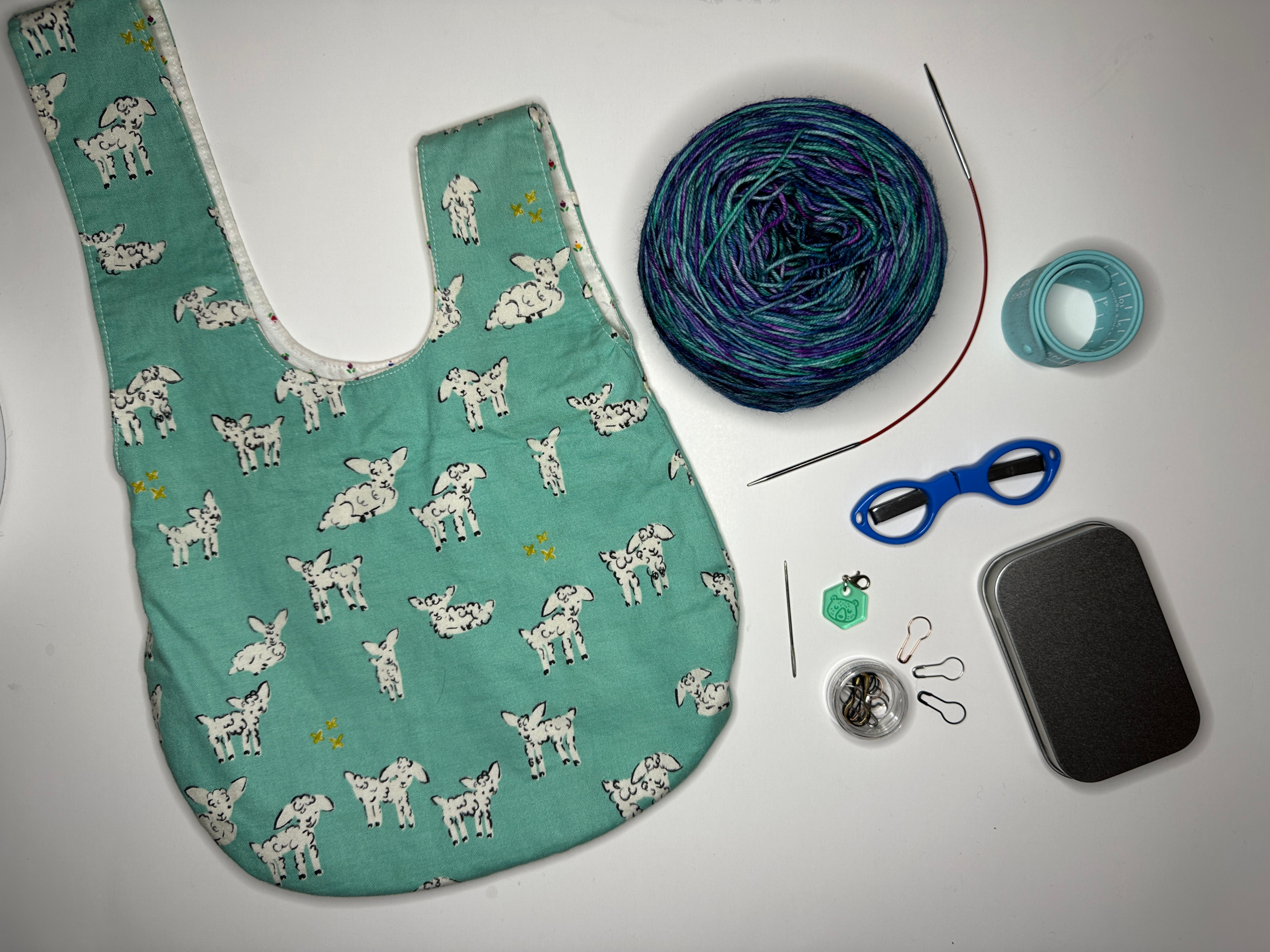 Project bag with yarn needles, scissors, stitch markers, ruler, darning needle and tin